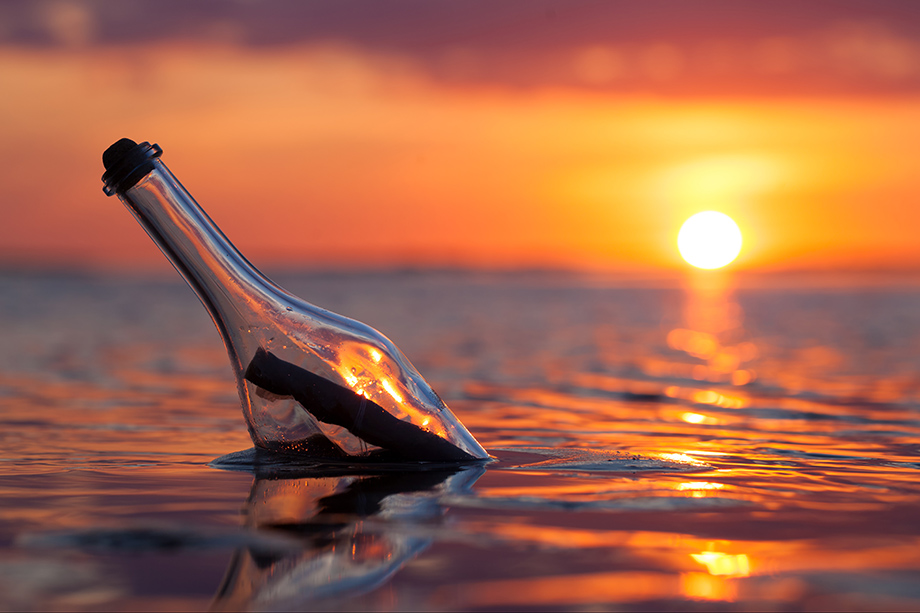 Garrafa de vidro com mensagem dentro boiando no mar, durante o por do sol